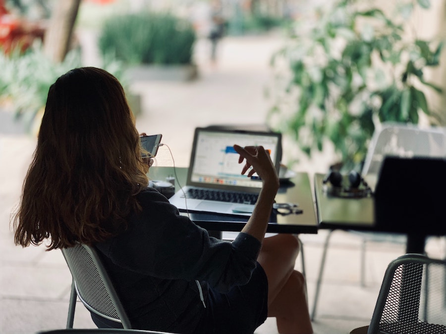 fille qui est assise sur une chaise et qui regarde son telephone avec en face d'elle son ordinateur